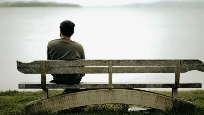 A person sits alone on a wooden bench by the water, capturing peaceful solitude