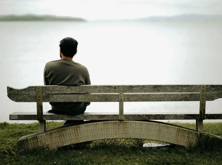 A person sits alone on a wooden bench by the water, capturing peaceful solitude